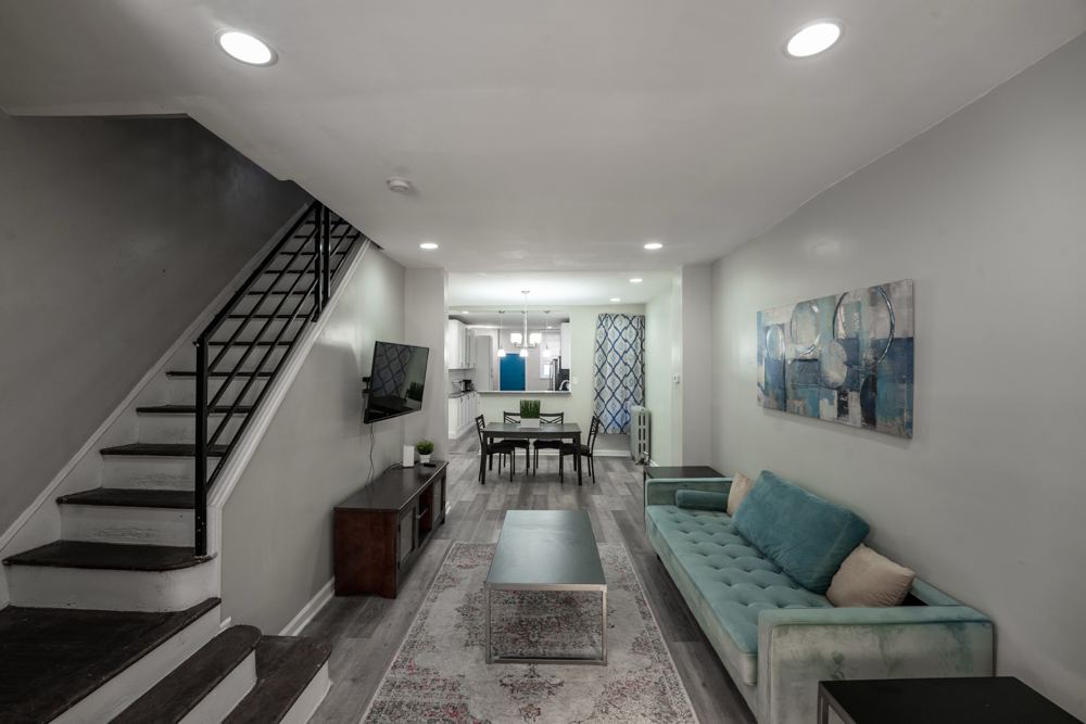 Furnished living room with a teal sofa, coffee table, wall-mounted TV and a staircase